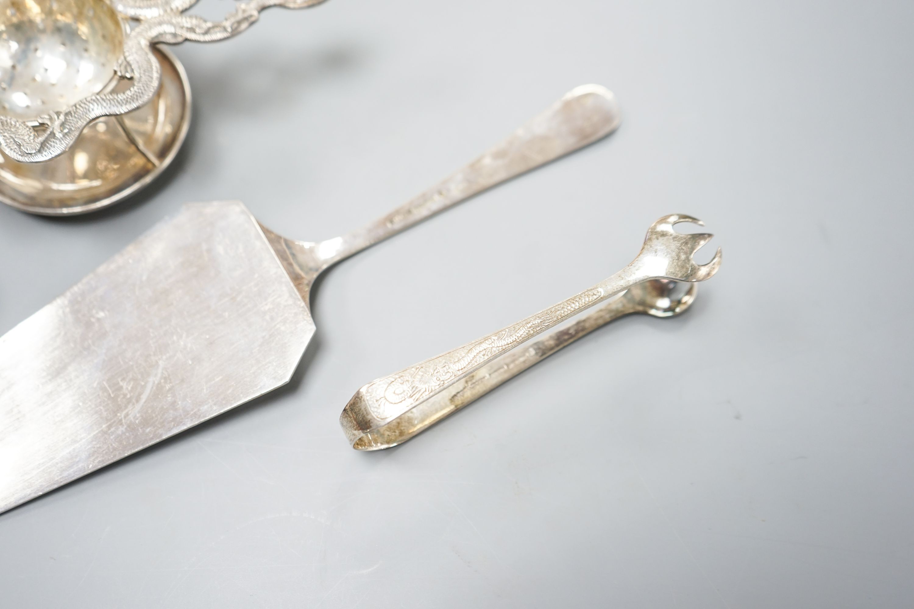 A Chinese white metal cake slice by Tack Hing, 24.4cm and a tea strainer on stand, pair of sugar tongs and pin cushion by Kingsburg, Hong Kong.